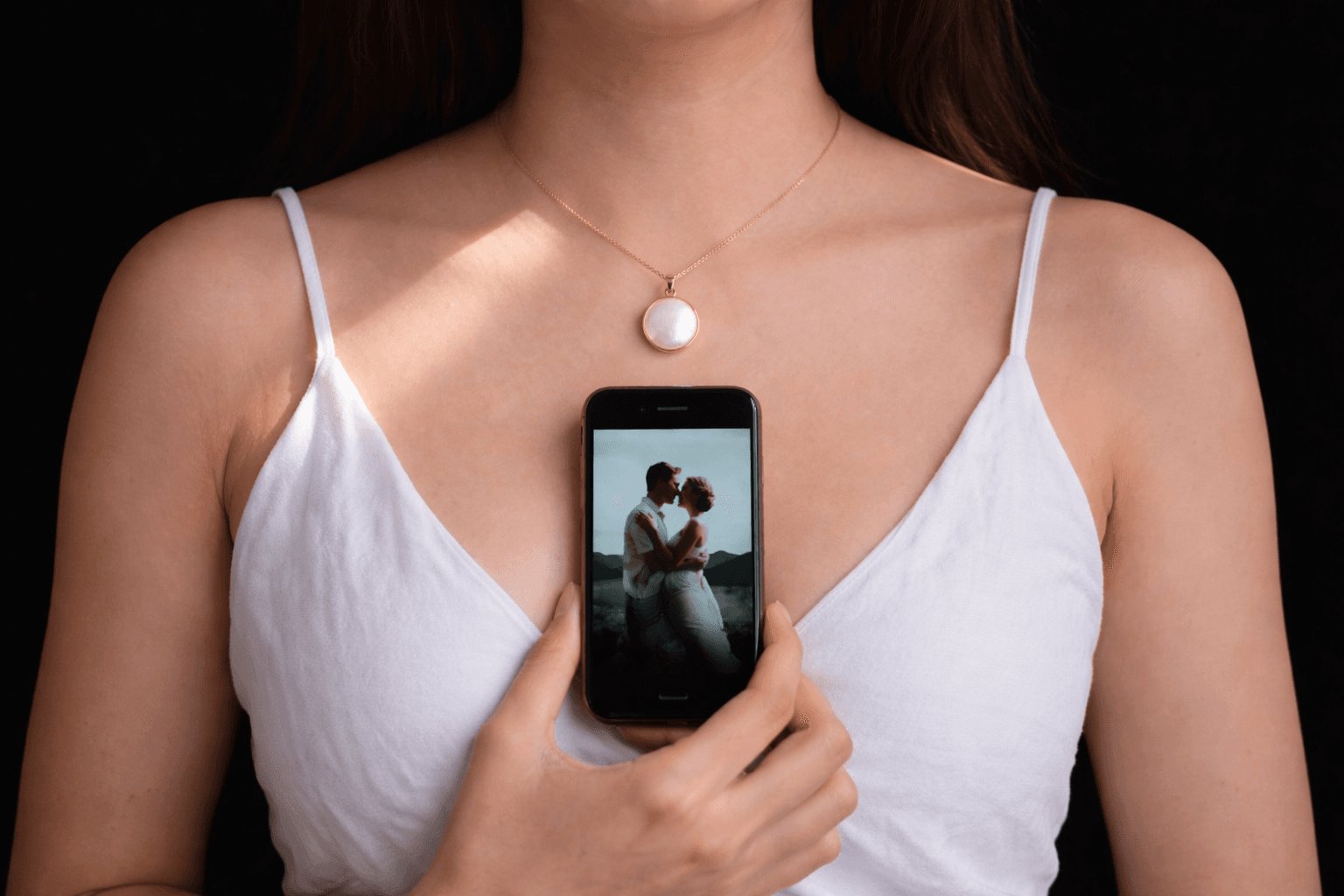 A gold Memoura pendant necklace with a phone displaying a cherished memory